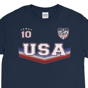 May include: Navy blue long-sleeve shirt with a red, white, and blue USA graphic. The shirt has a number 10 on the front and a small USA logo with stars.