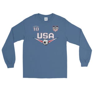 May include: A blue long-sleeve shirt with a white soccer jersey design. The shirt has the number "10" and the word "USA" with a soccer ball and a small USA flag.