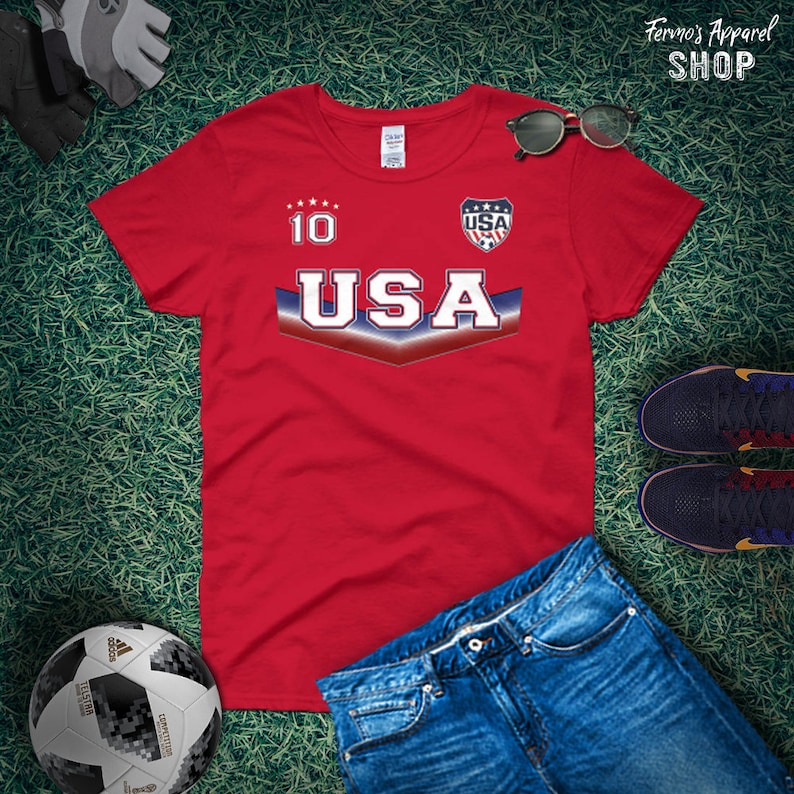 May include: Red t-shirt with a white "USA" graphic and a blue and red chevron design. The shirt also has a white "10" on the chest and a small "USA" logo on the right side.