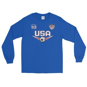 May include: A royal blue long-sleeve shirt with a white soccer ball and the text "USA" in a white, red, and blue font. The number "10" is printed in white above the text. A small USA flag is printed in the top right corner.