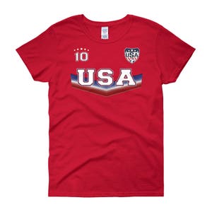 May include: Red women's t-shirt with a white and blue USA soccer jersey design. The shirt has the number 10 and the word USA on the front.