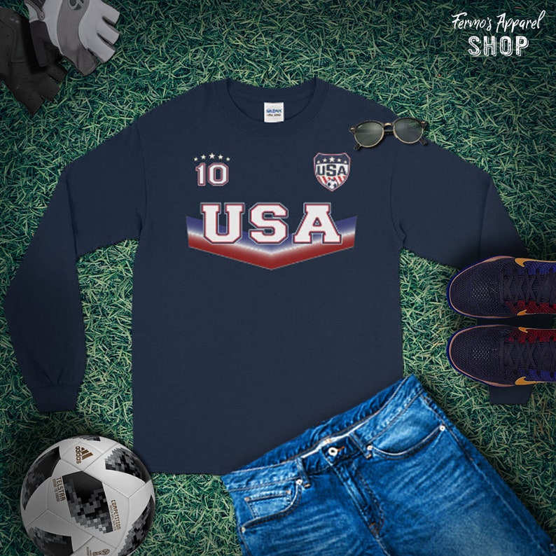 May include: Navy blue long-sleeve shirt with a white "USA" graphic and red, white, and blue stripes. The shirt has a white "10" on the left chest and a small shield with "USA" inside on the right chest.