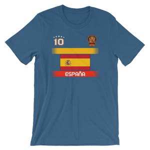 May include: A blue t-shirt featuring the Spanish flag design. The shirt has the number 10 and the word "Espa&ntilde;a" printed on it. The design includes a gold and red color scheme, with a crest on the upper right.