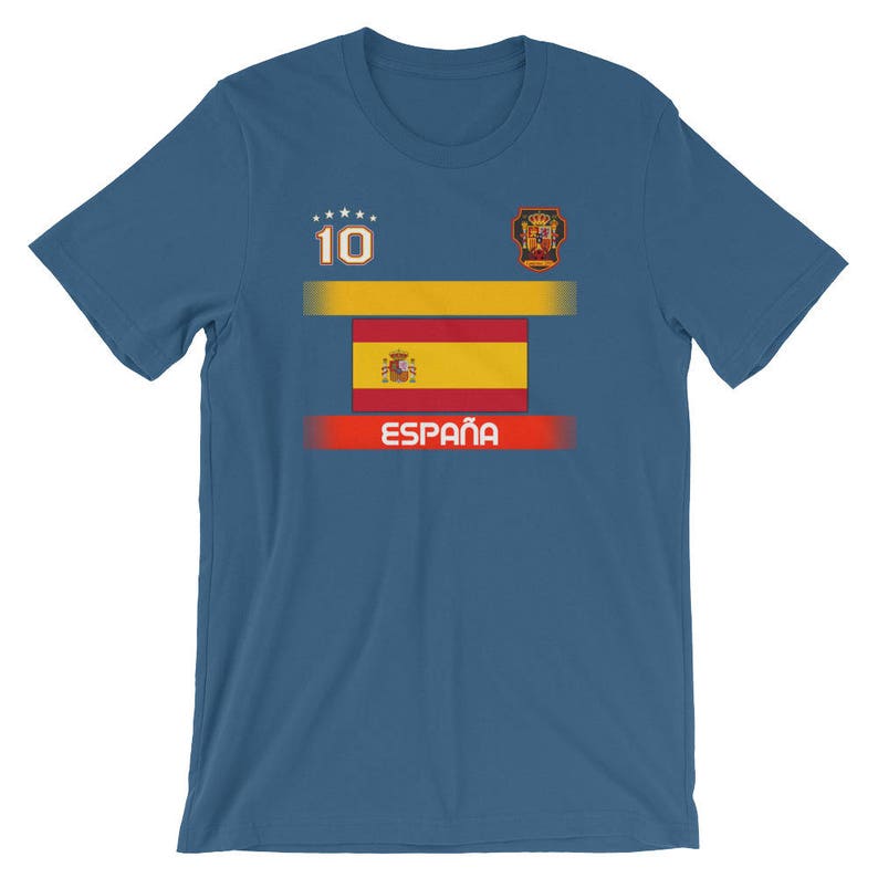 May include: A blue t-shirt featuring the Spanish flag design. The shirt has the number 10 and the word "Espa&ntilde;a" printed on it. The design includes a gold and red color scheme, with a crest on the upper right.