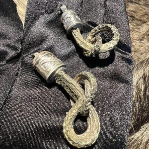 May include: Two silver and leather cord bracelets with decorative silver charms. The charms are round and have intricate designs. The leather cords are braided and knotted.