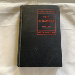 May include: A black hardcover book with the title "The Alhambra" by Irving. The book is part of the Academy Classics series and published by Allyn and Bacon.