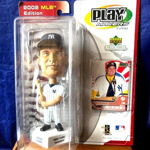May include: A New York Yankees Jason Giambi bobblehead from the 2002 MLB Edition, packaged in a clear plastic case. The bobblehead is wearing a Yankees uniform and holding a bat. A collectible card is also included.