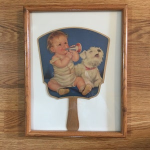 Abanico antiguo enmarcado con un bebé tocando el cuerno mientras el perro canta. Charlotte Becker, década de 1930