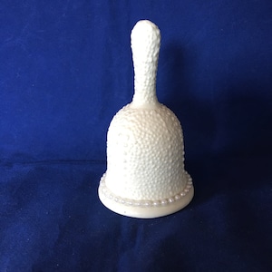 May include: A white ceramic bell with a textured surface and a pearl-like trim around the base.