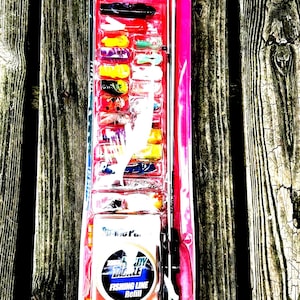 May include: A complete Zebco Ready Tackle fishing kit in a pink and clear plastic package. The kit includes a fishing rod, tackle, and fishing line refill. The package is on a weathered wooden surface. The text "Let's Fishing!" is visible.