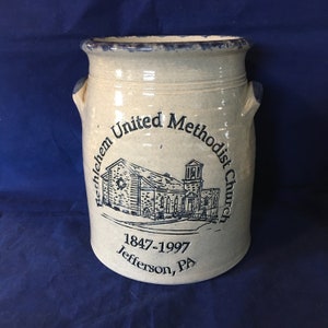 May include: A beige ceramic crock with a blue glaze around the top and handles. The crock has a black and white image of a church with the text "Bethlehem United Methodist Church 1847-1997 Jefferson, PA" around the image.