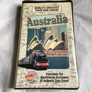 Może przedstawiać: Kaseta VHS z niebiesko-białą mapą świata na okładce. Tytuł to "World's Greatest Train Ride Videos", a podtytuł to "Australia". Obrazek przedstawia Operę w Sydney i pociąg.