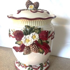 Peut inclure: Pot en céramique blanche avec un motif floral rouge, vert et blanc. Le pot a un couvercle avec un motif de pomme de pin.