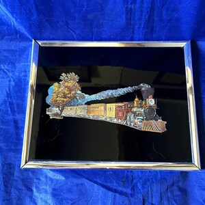 May include: A framed picture featuring a vintage train scene. The train, with its engine and colorful cars, is set against a black background. The frame is silver-colored, and the image includes a tree and a puff of smoke.