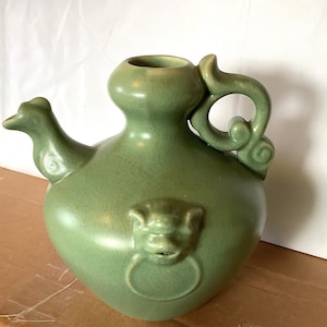 May include: A green ceramic teapot with a dragon head spout and a handle shaped like a cloud. The teapot has a decorative design on the front.