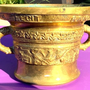 May include: A gold mortar and pestle with ornate carvings and two handles. The mortar has the inscription "FECIT A" on the top rim.