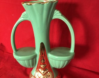 May include: A green ceramic vase with gold accents and two handles. The vase has a unique design with two small bowls on either side of the main vase.