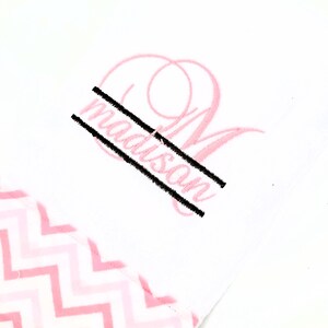 May include: White fabric with a pink chevron pattern and a pink monogram. The name "madison" is embroidered in black, with a large pink letter "M" in the background.