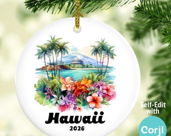 Puede incluir: Adorno navideño redondo de cerámica blanca con una ilustración de un paisaje hawaiano. La imagen incluye palmeras, flores y una montaña. La palabra "Hawaii" y el año "2026" están impresos en negro. El adorno cuelga de una cuerda dorada.