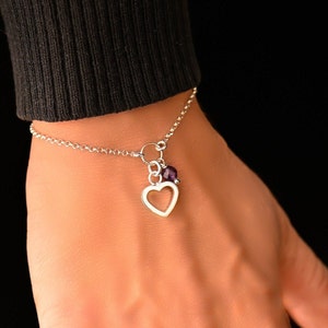 Può includere: Un braccialetto a catena d'argento con un ciondolo a forma di cuore aperto e una piccola pietra preziosa viola.