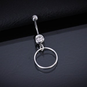Könnte beinhalten: Ein silberner Bauchnabelring mit einem klaren Kristall und einem silbernen Ring, der daran hängt.