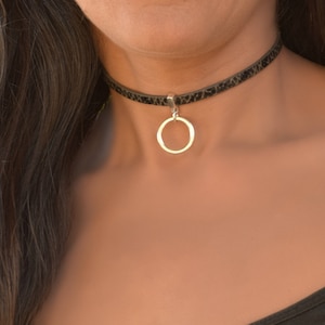 Op de afbeelding: Een zwarte leren choker met een zilveren ronde hanger.