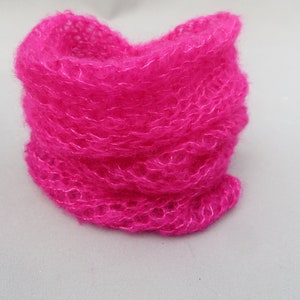 May include: A bright pink fuzzy knit scarf. The scarf is made of a soft, fluffy yarn and is folded in a circle.
