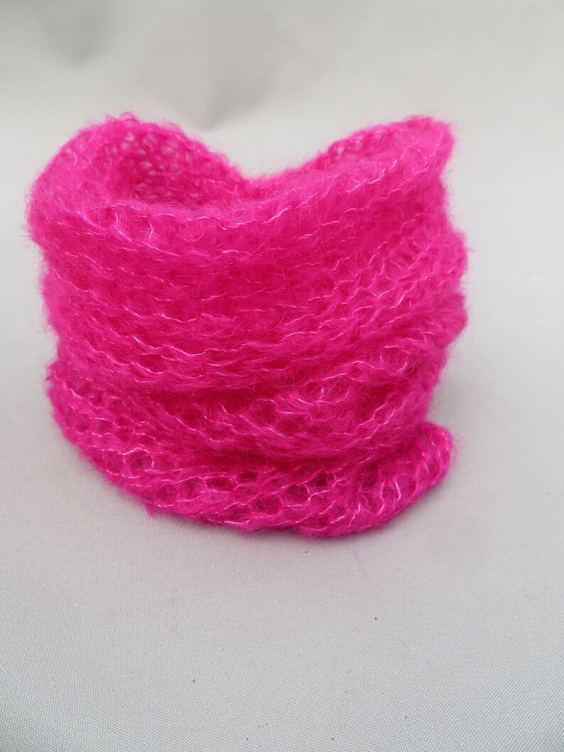May include: A bright pink fuzzy knit scarf. The scarf is made of a soft, fluffy yarn and is folded in a circle.