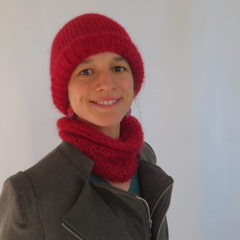 May include: A woman wearing a red knitted hat and matching scarf. The hat is slouchy and the scarf is a cowl style.