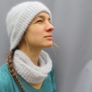 May include: A woman wearing a white knitted hat and a white knitted scarf. The hat and scarf are both very delicate and have a lacy appearance. The woman is looking up and to the right.