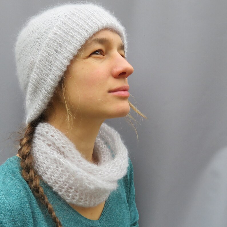 May include: A woman wearing a white knitted hat and a white knitted scarf. The hat and scarf are both very delicate and have a lacy appearance. The woman is looking up and to the right.