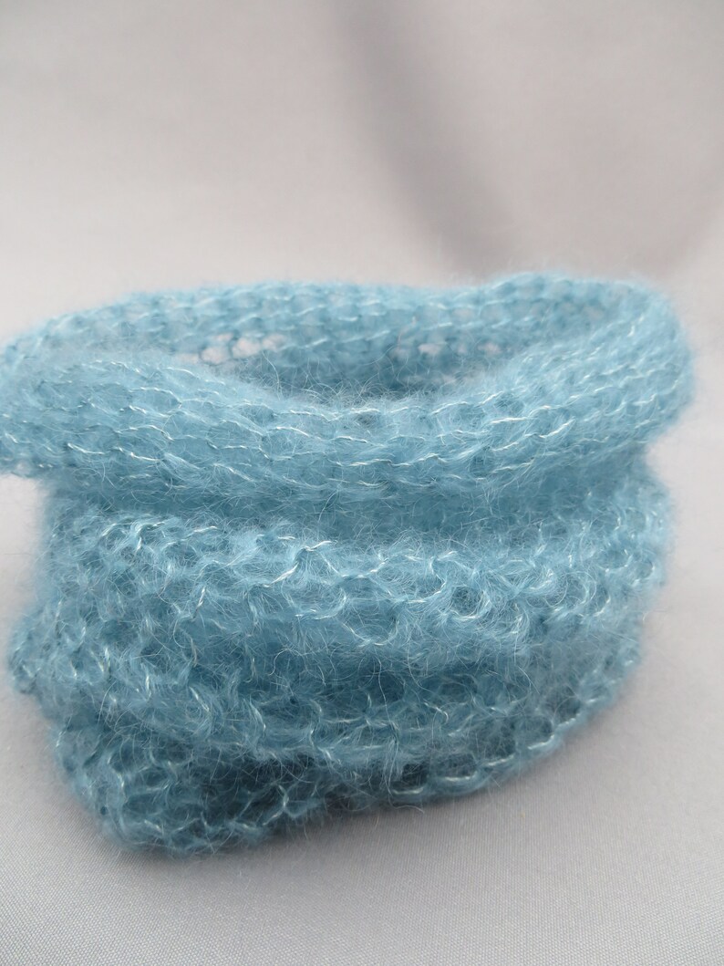May include: A soft, light blue knitted cowl made from a fuzzy yarn.