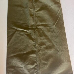May include: Olive green drawstring bag. The bag is made of a smooth, slightly shiny fabric. A white drawstring is visible at the top. The bag has a vertical seam down the centre.