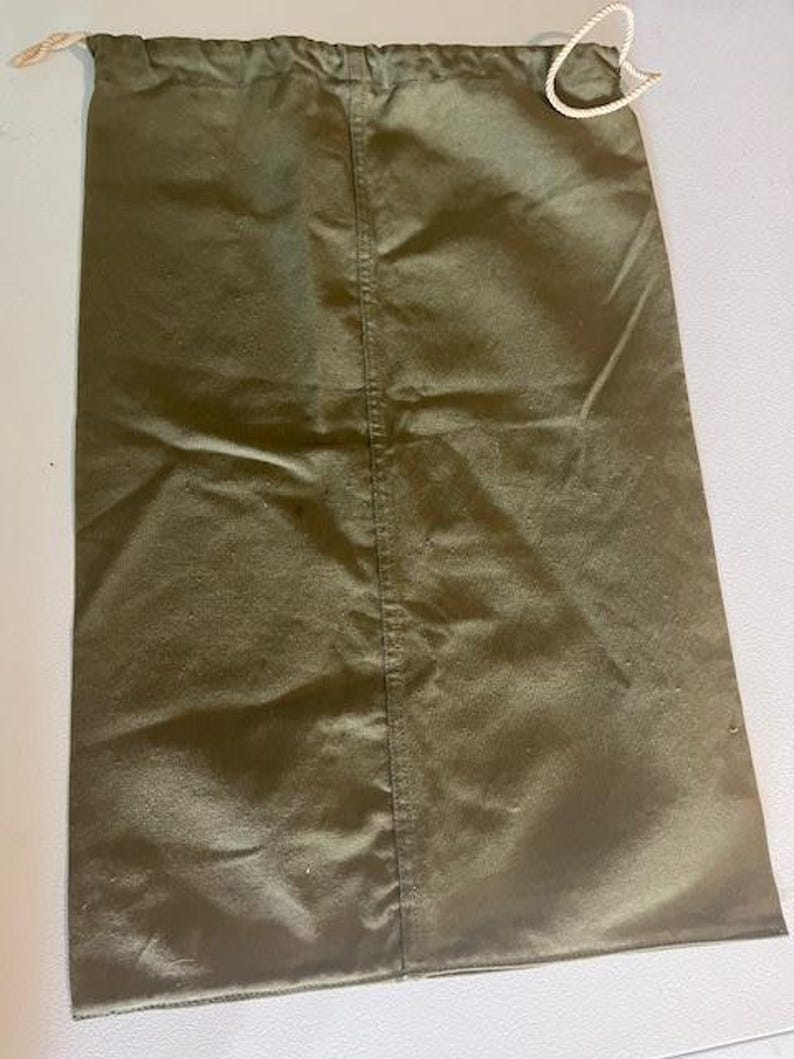 May include: Olive green drawstring bag. The bag is made of a smooth, slightly shiny fabric. A white drawstring is visible at the top. The bag has a vertical seam down the centre.