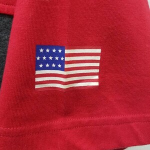 May include: Red t-shirt with a small American flag patch on the left sleeve.