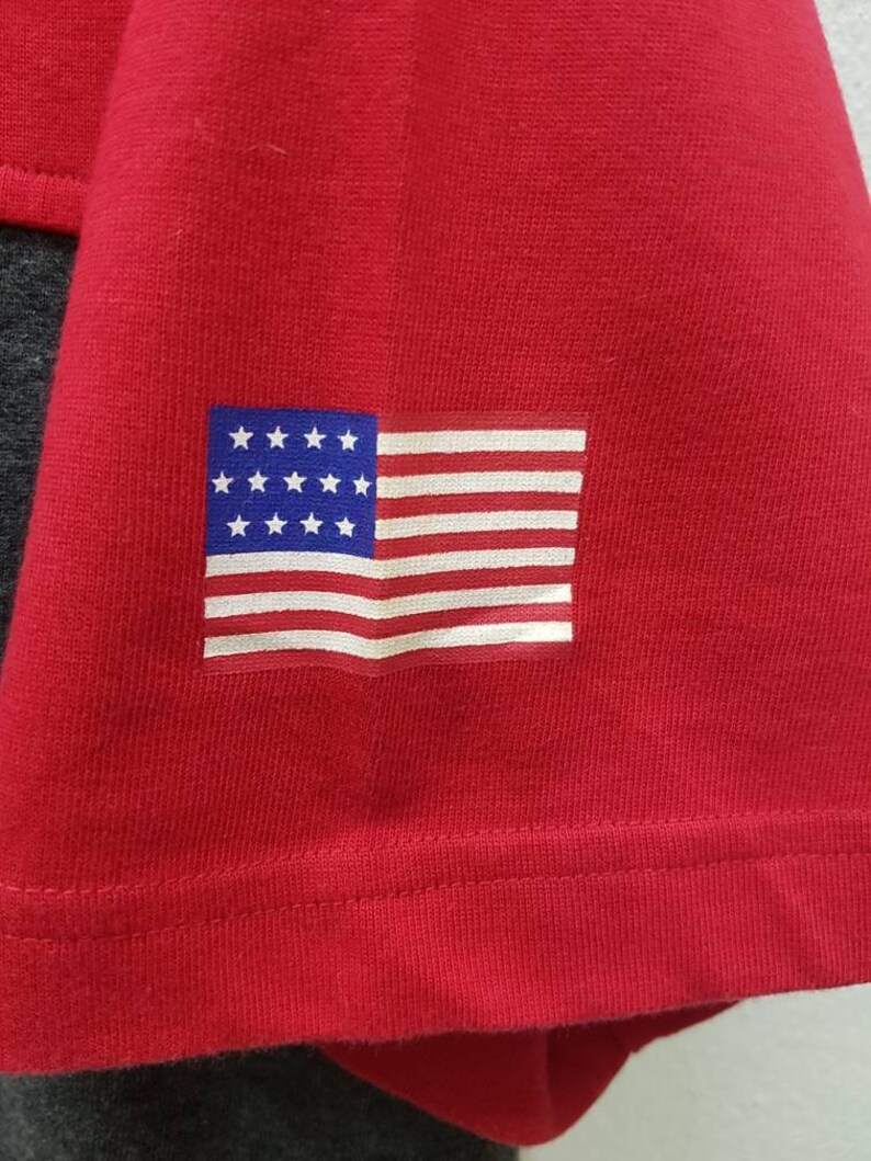 May include: Red t-shirt with a small American flag patch on the left sleeve.