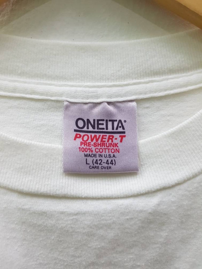 Puede incluir: Etiqueta blanca con texto negro que dice "ONEITA POWER-T PRE-SHRUNK 100% COTTON MADE IN U.S.A. L (42-44) CARE OVER"