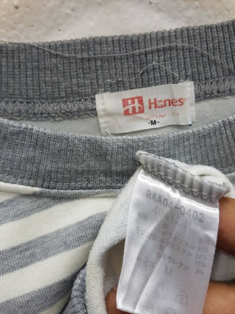 May include: Grey and white striped shirt with a Hanes label. The label says "Hanes" and "North Carolina, USA". The size is "M".