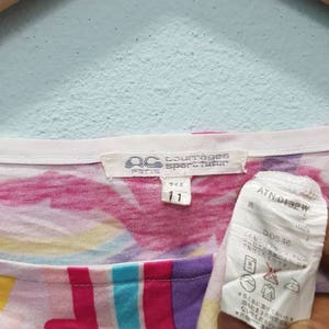 May include: A white, pink, yellow, blue, and purple patterned shirt with a white tag that says "Paris Sportwear" and "Size 11". The tag also has a black and white label with the text "ATN-0132 W" and "DOS 46".