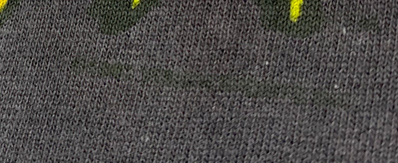 May include: Close-up of a dark gray fabric with a subtle texture. The fabric has a faint yellow pattern.