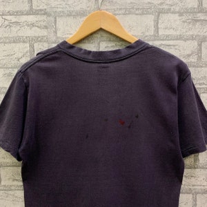 May include: A dark purple t-shirt with a crew neck and short sleeves. The shirt has a few small stains on the back.