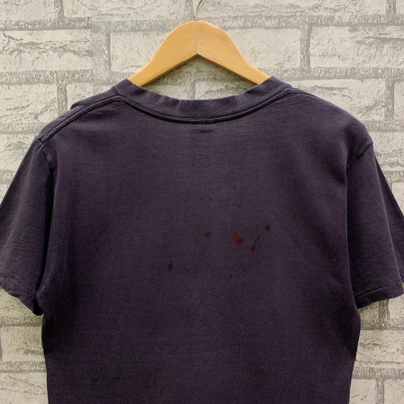May include: A dark purple t-shirt with a crew neck and short sleeves. The shirt has a few small stains on the back.