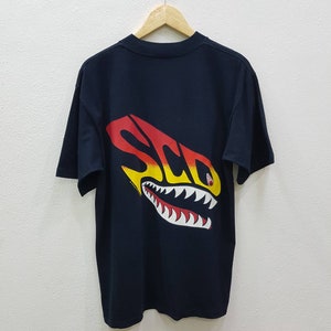 May include: Black t-shirt with a graphic of a shark with the word "SCD" in yellow, red, and orange on the back.