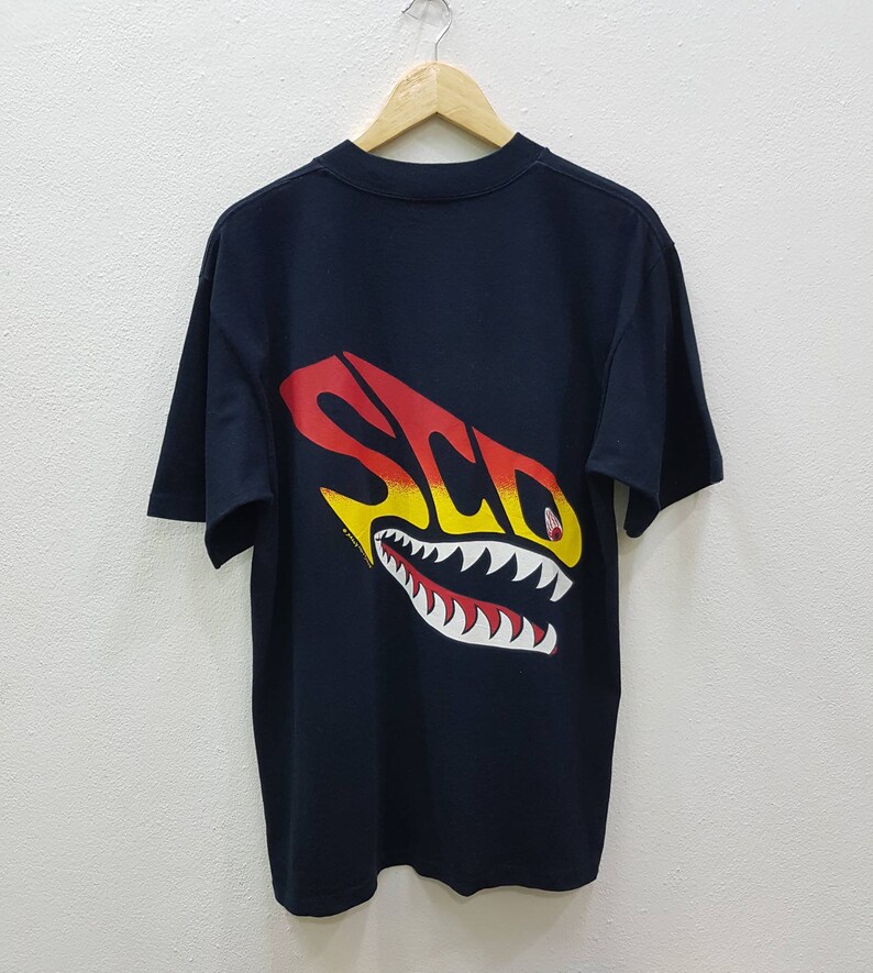 May include: Black t-shirt with a graphic of a shark with the word "SCD" in yellow, red, and orange on the back.