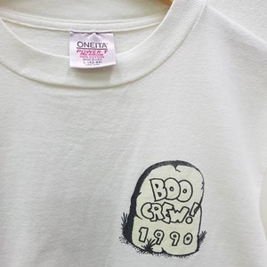 Puede incluir: Camiseta blanca con un gr&aacute;fico en blanco y negro de una l&aacute;pida con el texto "BOO CREW! 1990". La camiseta tiene una etiqueta que dice "ONEITA POWER-T PRE-SHRUNK 100% COTTON MADE IN USA L (42-44) CARE OVER"