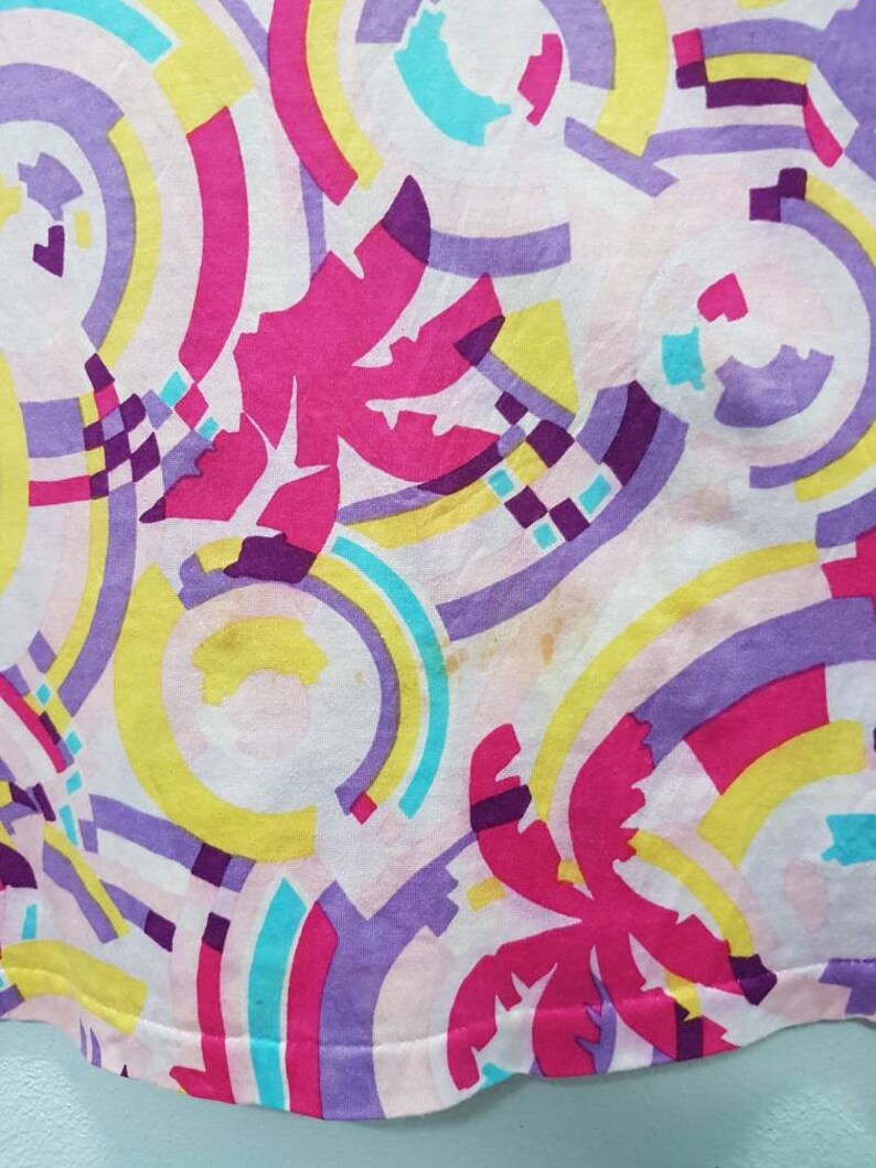 May include: A pink, yellow, blue, and purple fabric with a geometric pattern of circles and palm trees.
