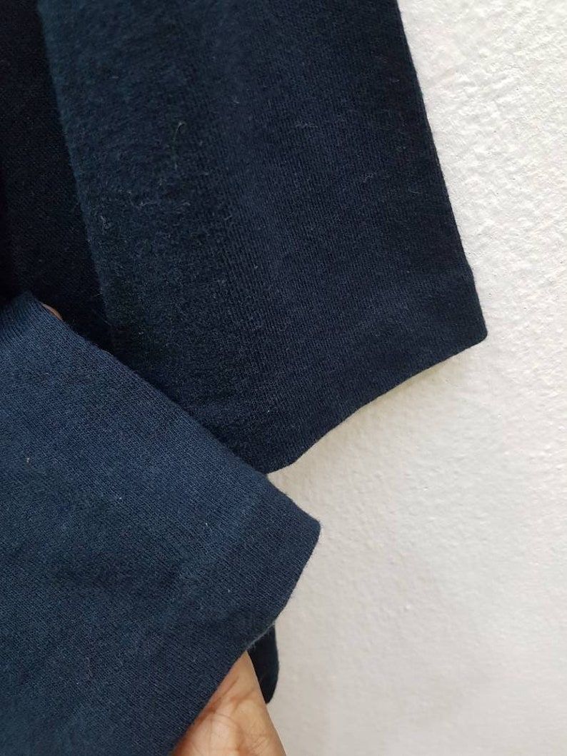 May include: Close-up of the navy blue fabric of a long-sleeved shirt. The fabric is soft and has a slight texture.