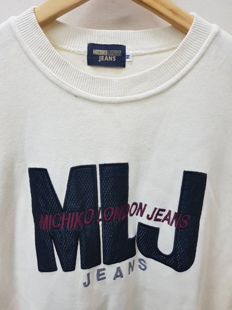 May include: White long-sleeve sweatshirt with a black and white embroidered logo that says "Michico London Jeans" and "Jeans" in a smaller font.