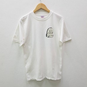 Puede incluir: Camiseta blanca de manga corta con un gr&aacute;fico en blanco y negro de una l&aacute;pida con el texto "B.D.D. Crew 1998" en ella.