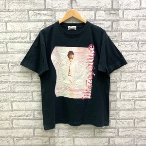 Puede incluir: Camiseta negra con un gráfico rosa y blanco de un hombre con el texto "Kazuya" y "Ken Segawa" impreso en ella.